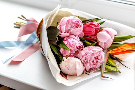 Bouquet of pink peonies in craft paper on white windowsill - gift for girlの写真素材
