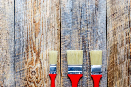 three paint with red grips brush on wooden floor top view
