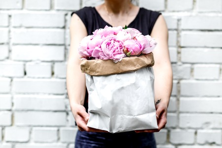 woman with bouquet of pink peonies in kraft bag on background of a brick wallの写真素材