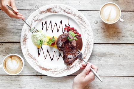Sweet dessert with coffee on the wooden table with hands top viewの写真素材
