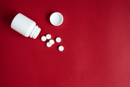 tablets in plastic container on red background top view