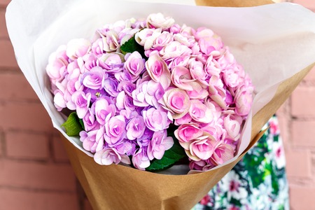 woman with bouquet of pink flowers in kraft paper on background of a brick wallの写真素材