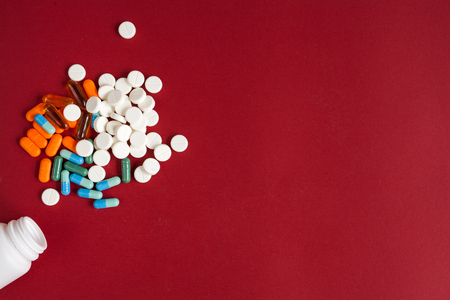 colored tablets in plastic container on red background top viewの写真素材