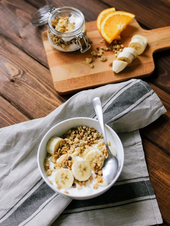 healthy breakfast bowl of yogurt with granola and banana on dark wooden backgroundの写真素材