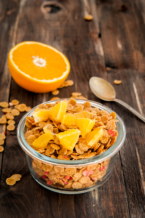 flakes in bowl with orange slices on dark wooden background.
