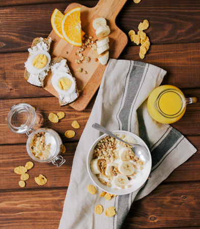 healthy breakfast bowl of yogurt with granola and banana, eggs on dark wooden background top viewの写真素材