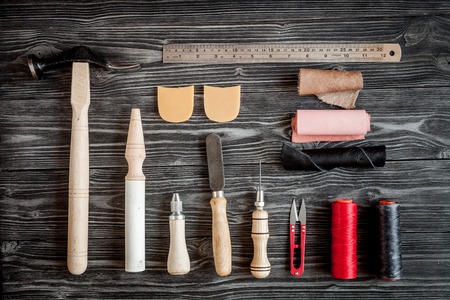 Instruments in leather shop on dark wooden background top view.