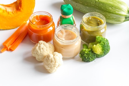 baby mashed with spoon in glass jar on white backgroundの写真素材