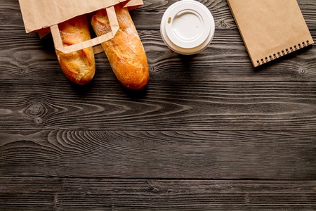 cup coffee and bread in paper bag on wooden backgroundの写真素材