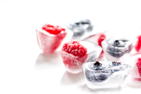 frozen blueberry and raspberry in icecubes on white backgroundの写真素材