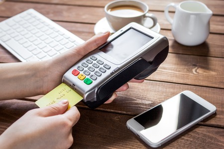 Payment by credit card in cafe with terminal and keyboard on wooden desk background