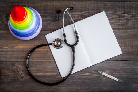 stethoscope, thermometer, opened notebook on children's doctor office wooden desk background top view mockupの写真素材