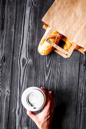 cup of coffee and bread in paper bag on wooden backgroundの写真素材