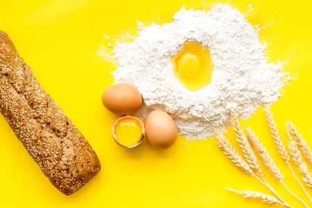 Make bread concept. Bread near wheat ears, flour and eggs on yellow top view