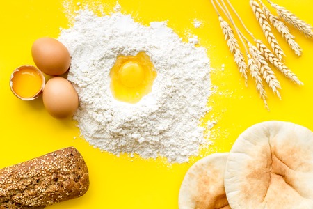 Make bread concept. Bread near wheat ears, flour and eggs on yellow background top viewの写真素材