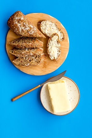 Wholegrain bread on cutting board with butter on plate, slice of bread with butter on blue background top viewの写真素材