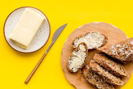 Traditional breakfast. Wholegrain bread on cutting board with butter, slice of bread on yellow background top viewの写真素材