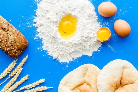 Ingredients for homemade bread. Bread near wheat ears, flour and eggs on blue background top viewの写真素材