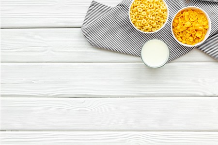 Various corn cereals in bowls and milk on white wooden background top view copyspace