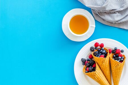 Light breakfast with fresh berries in waffle cones and cup of tea on served blue kitchen table...