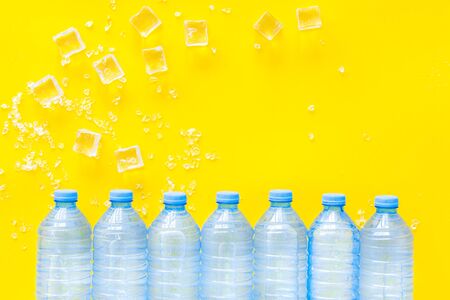 Cold pure water in plastic bottles with ice cubes on yellow  top view mockupの写真素材