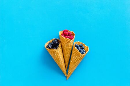 Summer design. Fresh berries in waffle cones on blue top view mock upの写真素材