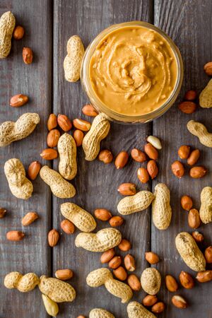 Product for hearty breakfast with peanut butter in bowl near nuts on wooden background top view patternの写真素材