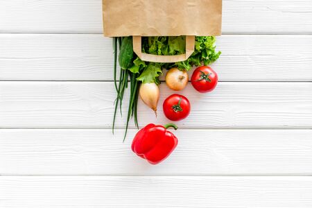 Healthy food with fresh vegetables in paper bag on white wooden background top view