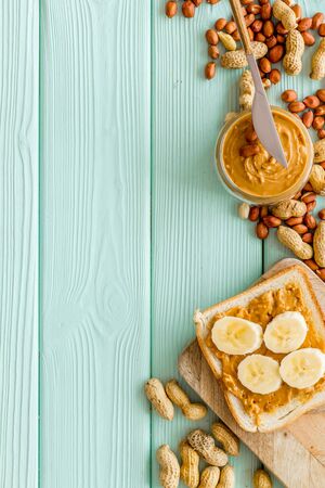 Vegan breakfast. Make sandwiches with banana and peanut butter in glass bowl, knife on mint green wooden background top view copyspaceの写真素材