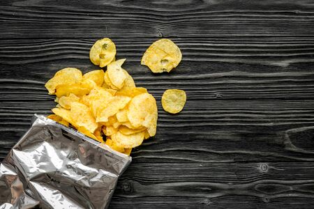 Fastfood. Bag of homemade potato chips for snack on wooden background top view copyspace