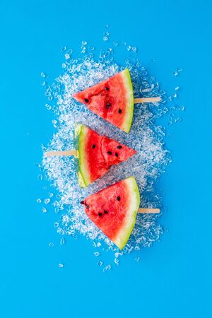 Cut watermelon on ice with fruit popsicle on blue background top viewの写真素材