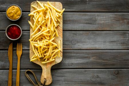 Fast food restaurant concept. French fries on cutting board near sauces on wooden table top-down copy spaceの写真素材