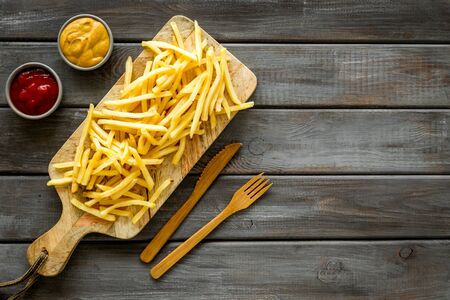French fries on cutting board near sauces on wooden table