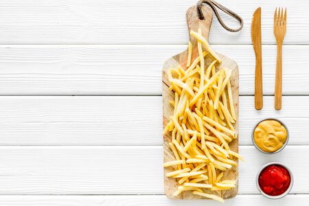 French fries on cutting board near sauces on white wooden table top-down copy space