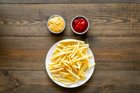 Fast food symbol. French fries on plate on dark wooden table top-down.