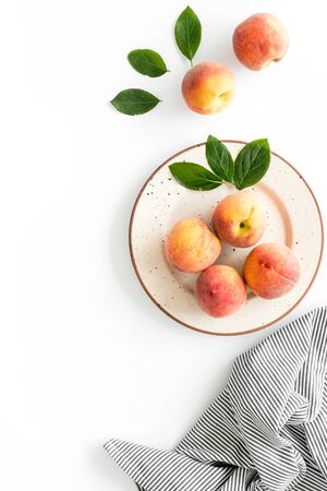 Summer lunch. Red peaches on white background with tablecloth and leaves top-down.の写真素材