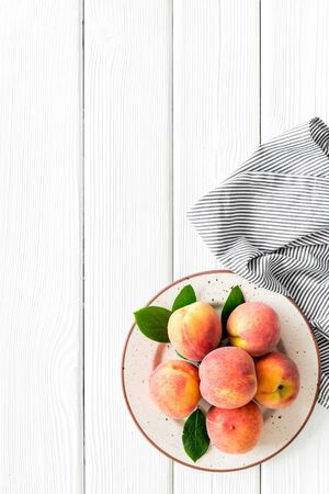 Summer lunch. Red peaches on white wooden background with tablecloth and leaves top-down copy spaceの写真素材
