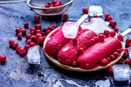 ice, red berries and popsicle on dark desk background