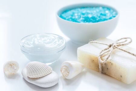 blue bath salt, body cream and shells for spa on white table background