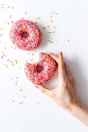Hand holding donut with icing and sprinkles. Flat lay, top view