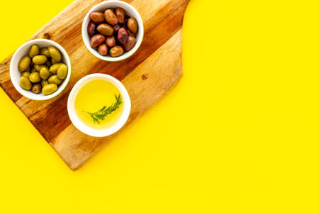 Olives and olive oil in bowls on cutting board on yellow top view copy space