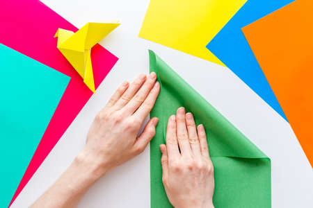 Female hands folding sheet of paper - origami bird. Overhead viewの写真素材