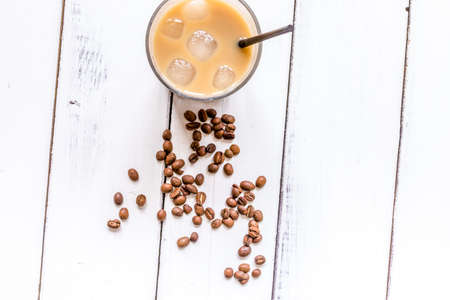coffee break with cold iced latte and beans on white table background top view