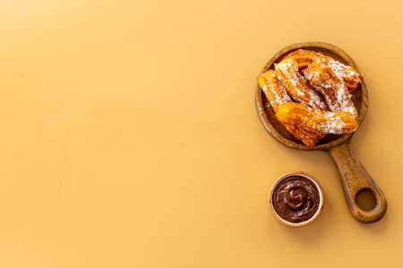 Plate with fried churros and chocolate sauce, top view
