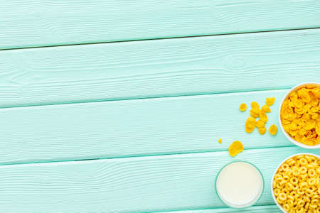 Corn cereals in bowls with milk on mint green wooden background top view space for text