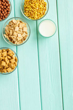 cereals, oatflakes and cornflakes with milk for healthy breakfast on mint wooden background top view...