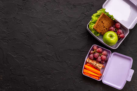 Student meal in purple lunch boxes filled with sandwich and fruitsの写真素材