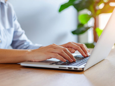Close-up of businesswoman hands typing on laptop keyboard in officeの素材