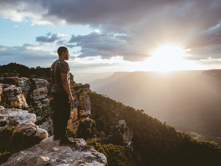 Man with backpack standing on top of the mountain and looking at the sunset.の素材