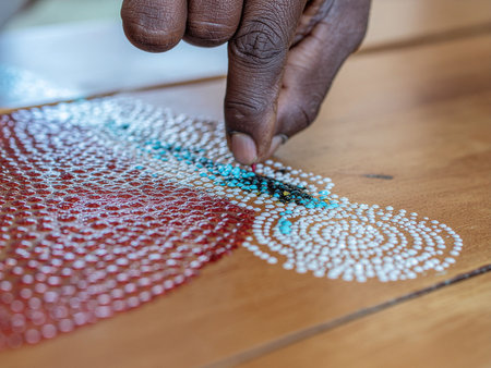 Close up of the hand of a man embroidering beads on wooden tableの素材
